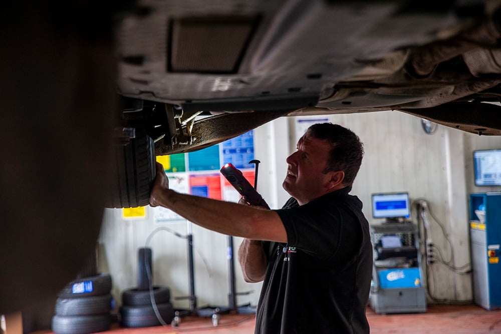 mechanic inspecting under car on ramp