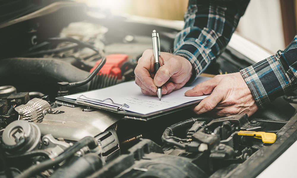 mechanic with clipboard writing above the car engine