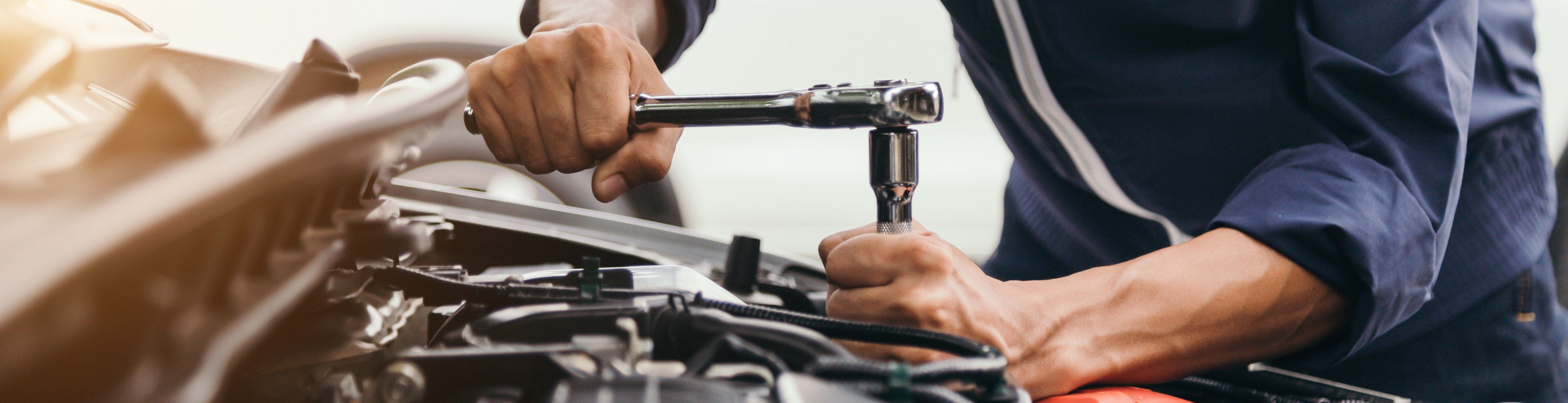 Mechanic working in the bonnet of a car with a tool